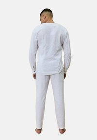 Chemise en lin blanche à manches longues, vue de dos. Associée à un pantalon en lin blanc assorti. Tissu léger, coupe décontractée, texture minimale.