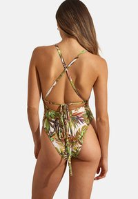 Maillot de bain une pièce avec un imprimé de feuilles tropicales, bretelles croisées réglables, dos nu, taille nouée et ouvertures de jambe à taille haute.