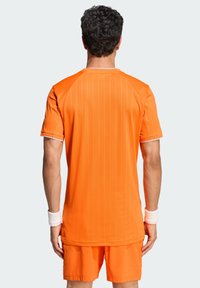 Πορτοκαλί αθλητική μπλούζα με κάθετες ρίγες, κοντά μανίκια και στρογγυλή λαιμόκοψη, συνδυασμένη με αντίστοιχα σορτς. Υφή υφάσματος.