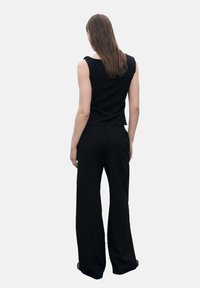 Top noir sans manches associé à un pantalon large taille haute noir. Tissu doux avec une coupe décontractée, design minimaliste et sans motifs visibles.