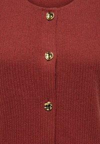 Σκούρο κόκκινο υφαντό ύφασμα με τρία γυαλιστερά, ακανόνιστα χρυσά κουμπιά ευθυγραμμισμένα κάθετα στο κέντρο.