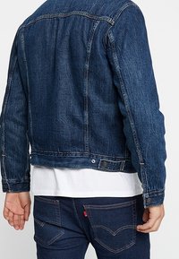 Mörkblå denimjacka med klassisk skärning, knäppning fram, synliga sömmar och en lätt sliten textur på tyget.