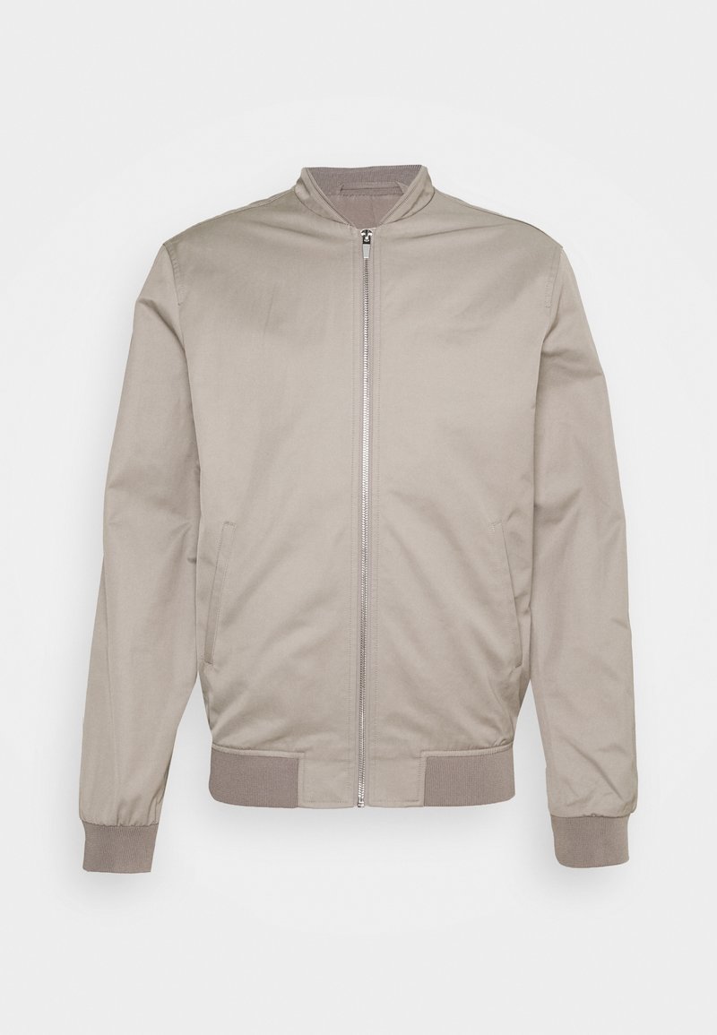 Giacca bomber beige chiaro realizzata in tessuto liscio, con zipper frontale, polsini e orlo a costine, e due tasche laterali.