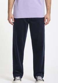 Pantalons en velours côtelé bleu marine avec une coupe droite, featuring des côtes verticales et une texture douce, associés à des baskets noire et blanche.