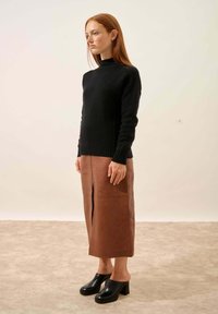 Czarny sweter dzianinowy z wysokim kołnierzem, brązowa skórzana midi spódnica z rozcięciem z przodu, czarne sandały na obcasach z odkrytymi palcami i grubymi obcasami.