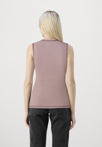 Ribbad ärmlös topp i dammrosafärg med rund halsringning och en figurnära silhuett, tillsammans med högmidjade mörka byxor.