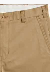 Pantalones beige de tejido texturizado con un sutil patrón diagonal. Cuenta con cierre de botón y trabillas en la cintura.