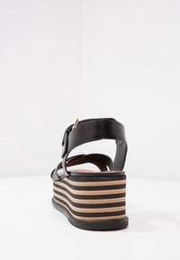 Black leather wedge sandal with a strappy design, featuring a striped cork platform and a silver buckle detail.