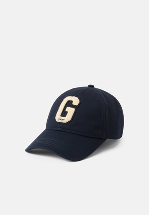 Gorra de béisbol azul marino con un suave parche en crema con la letra 'G' en la parte frontal y costuras detalladas. Cuenta con un visor curvado y una correa ajustable.