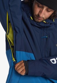 Marinblå och blå vattentät jacka med mesh-foder, justerbar huva och dragkedjedetaljer. Har en kroppsnära manschett och logotypaccent.