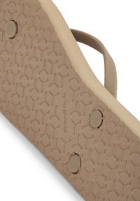 Svetlohnedá podrážka flip-flop sandálov s textúrovaným grip vzorom. Obsahuje malé kruhové kovové akcenty a žiadne viditeľné logá alebo štítky.
