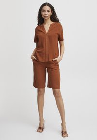 Outfit color ruggine composto da una camicia a maniche corte con bottoni e pantaloni shorts fino al ginocchio, realizzato in un tessuto testurizzato con vestibilità rilassata.