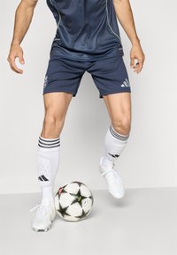 Laivyno spalvos sportiniai šortai su šviesiomis juostelėmis, derinami su baltais kojiniais su juodais akcentais. Po kojomis yra balta futbolo kamuolys su žvaigždžių raštais.