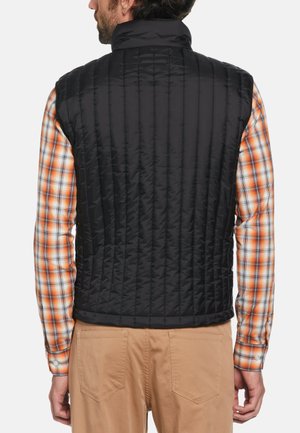 Schwarweste mit Steppdesign und Stehkragen, mit vertikalen Nähten und seitlichen Taschen, getragen über einem karrierten, orange-weißen Langarmhemd.