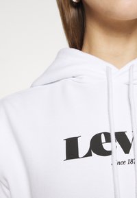 Felpa bianca con un grande logo nero "LEVI'S", cordini regolabili, tessuto testurizzato e una vestibilità comoda.