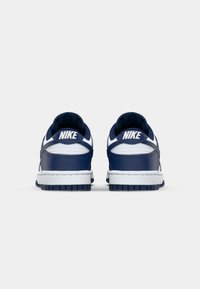 Navy ja valkoiset Nike-tennarit ovat varustettu nahkaisella päällisellä, pehmustetulla nilkkakappaleella ja kumipohjalla, jossa on kuvioitu pinta. Logo on näkyvissä kantapäässä.
