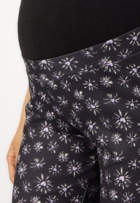 Leggings noirs avec un motif floral comprenant des fleurs violettes et blanches. Tissu lisse et extensible avec une large ceinture.
