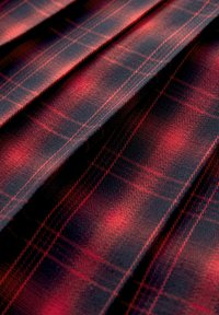 Red and black tartan fabric with a check pattern, featuring a smooth texture and pleated design, showcasing depth and color contrast.