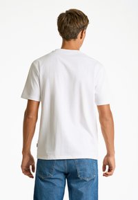Vit bomull t-shirt med korta ärmar och rund halsringning, ihop med blå denimjeans. Ingen synlig märkning eller mönster.
