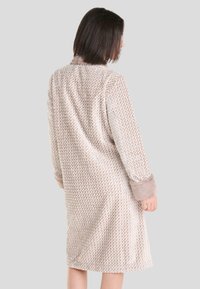 Túnica larga, beige, con un diseño de espiga, textura suave y puños de felpa en contraste. Cuello simple y ajuste ligeramente holgado.