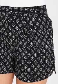 Shorts negros con una tela texturizada que presenta un patrón geométrico blanco de cuadrados y puntos. Incluyen una cinturilla y aberturas laterales.