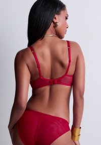 Ensemble de lingerie rouge en tulle et satin, doté de bretelles réglables et d'une fermeture à crochet, mettant en valeur une texture lisse et transparente.