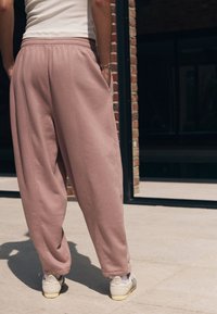 Roze trainingsbroek met een ontspannen pasvorm en elastische tailleband, voorzien van zijzakken en gecombineerd met witte en grijze sneakers.
