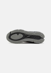 Black athletic shoe sole with a textured gray rubber surface, featuring deep grooves for traction and a slightly curved shape.