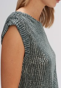 Blouse à motifs verts et crème, col rond, manches courtes avec un léger détail froncé, fabriquée en tissu léger.