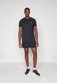 Sort atletisk t-shirt med korte ærmer og rund halsudskæring, parret med matchende shorts, båret med sorte sneakers og hvide sokker.