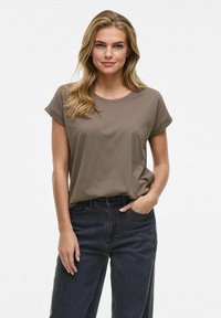 Camiseta de algodón marrón con mangas cortas y enrolladas, escote redondo y ajuste holgado, combinada con unos vaqueros oscuros de cintura alta.