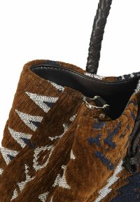 Texturiertes braunes Stoff-Tragetasche mit weißen und blauen geometrischen Mustern, schwarzem Lederinneren und einem geflochtenen Griff. Silberne Hardware-Details im Inneren.