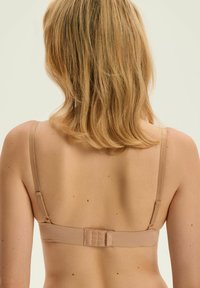 Beige wireless bra with adjustable straps, smooth texture, and hook-and-eye closure at the back. Subtle stitching detail along edges.