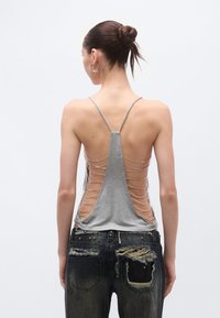 Halli top, millel on peened õlapaelad ja madal seljaosa, kaunistatud kettidega. Kombineeritud kulunud siniste teksapükstega.