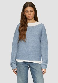 Lichtblauwe gebreide trui met een brede halslijn, lange mouwen en ribbeltextuur, gedragen over een wit shirt; casual, losse pasvorm.
