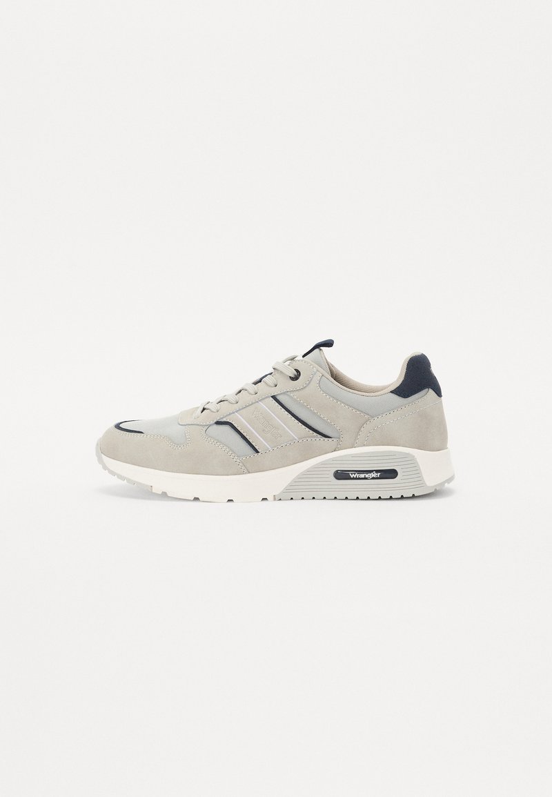 Grå mockasneakers med nätdetaljer, med tre randiga accenter i mörkare grått, en kraftig vit sula och en svart logotyp på hälen.