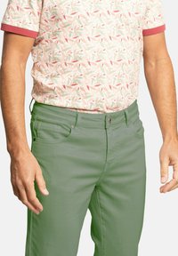 Pantalones de algodón verdes con un corte ajustado, que presentan bolsillos delanteros y un cierre de botón. Combinados con una camisa de manga corta con estampado floral.