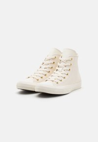 Witte hoge sneakers van canvas, met gouden oogjes, ronde neus, gestructureerde rubberen zool en platte veters. Eenvoudig ontwerp zonder patronen.