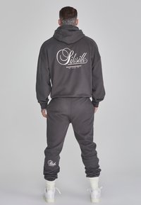 Felpa con cappuccio in cotone nero e pantaloni coordinati in tessuto morbido. Cappuccio con logo sul retro, polsini e caviglie sagomati, accentuati da un brand bianco.