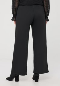 Pantaloni neri a gamba larga realizzati in tessuto morbido, con vita alta e vestibilità rilassata, abbinati a stivali neri con tacco alla caviglia.