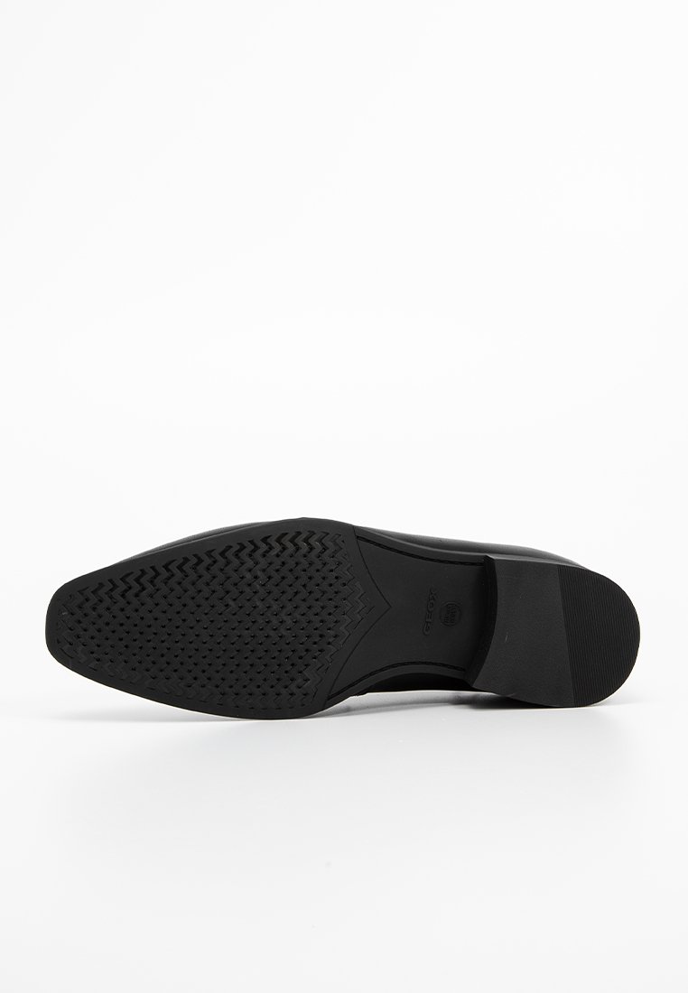 Czarna podeszwa buta wykonana z gumy, z teksturowanym wzorem dla lepszej przyczepności, o eleganckim, opływowym kształcie i lekko uniesionej pięcie.