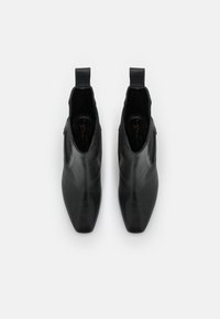 Botas de tobillo de cuero negro con punta afilada, paneles laterales elásticos y tiradores en el talón. Textura suave con un diseño minimalista.