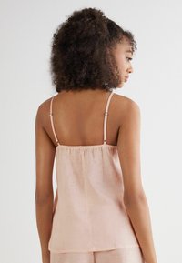 Top de tirantes espagueti en color rosa claro, hecho de una tela suave, con un diseño de espalda fruncida y un ajuste suelto y fluido. Diseño simple con detalles mínimos.