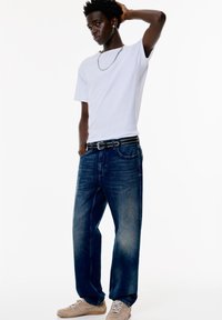 Vit bomulls t-shirt, mörkblå raka jeans med blekt tvätt, svart nittad bälte och ljusbeige sneakers. En enkel, avslappnad outfit.