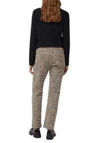 Jeans a stampa leopardato in color beige con un design a gamba dritta, accentuati da macchie scure, abbinati a un top nero a maniche lunghe.