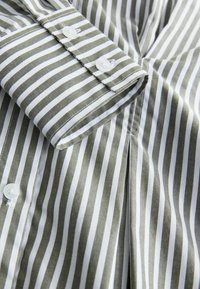 Striped shirt with green and white patterns, featuring buttoned cuffs, a smooth texture, and a neatly finished hem.