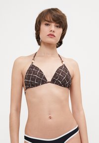 Rjav bikini vrh z belim mrežastim vzorcem, trikotne skodelice, zbrani stranski deli in vrvni vezi. Ima dekorativne perle na naramnicah.