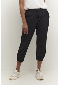 Zwarte cropped broek van lichtgewicht stof met een elastische tailleband, verstelbare trekkoord en elastische boorden. Gecombineerd met witte sneakers.