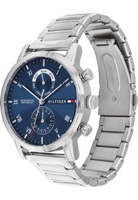 Montre en acier inoxydable argenté avec un cadran bleu foncé, index en chiffres romains, trois sous-cadrans et un bracelet en métal brossé. Comprend une fonction date.