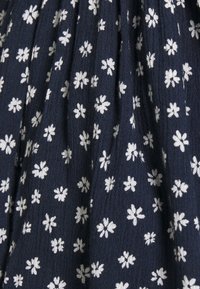 Marinblått tyg med ett upprepande mönster av små, vita blommotveller. Texturen verkar mjuk och något skrynklig.